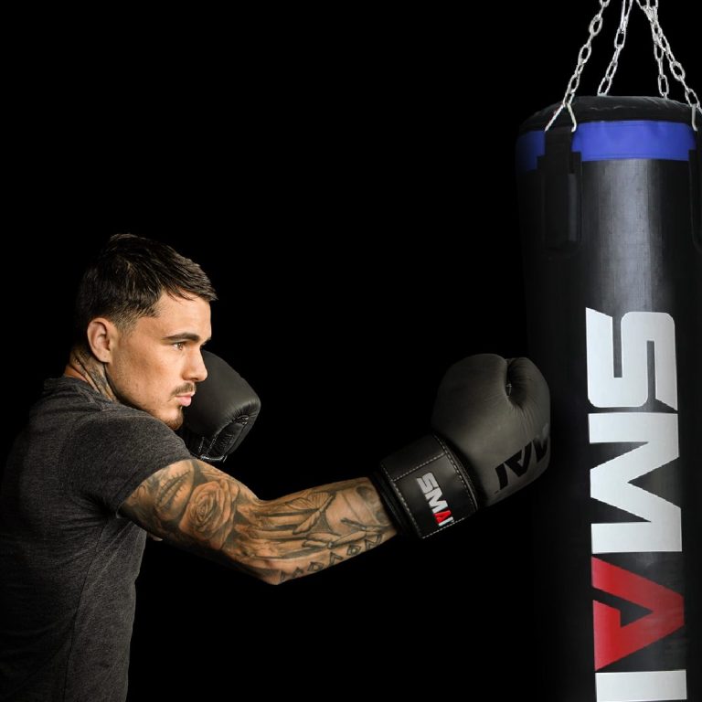Kick-/Boxen Boxer mit SMAI Boxhandschuhen schlägt einen SMAI Boxsack in einer dunklen Umgebung.