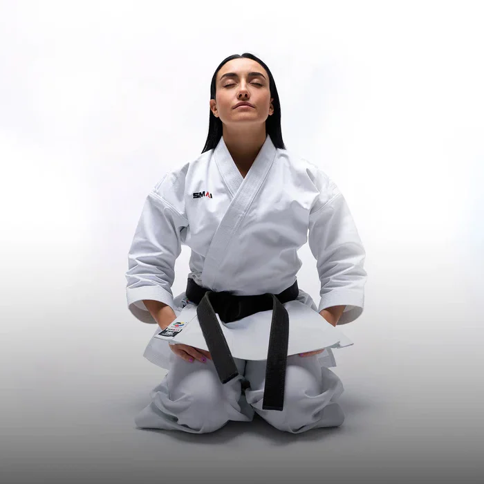 Kategorie - Karate Eine Person in Karate-Uniform von SMAI mit schwarzem Gürtel, in der Kniestellung.