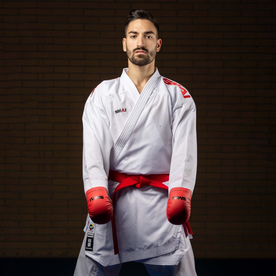 Inazuma Suit Pack Karateka im SMAI INAZUMA Karateanzug mit rotem Gürtel und roten SMAI Faustschützern.